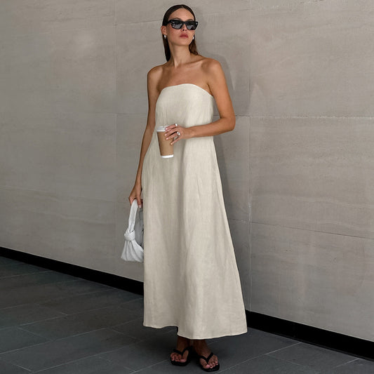 Model posing in the French Faux Linen Backless Maxi Dress, looking off into the distance with black sunglasses, holding a cup of coffee and a white handbag. The dress features a strapless neckline, A-line silhouette, smocked detailing, and pockets, offering timeless elegance and functionality.